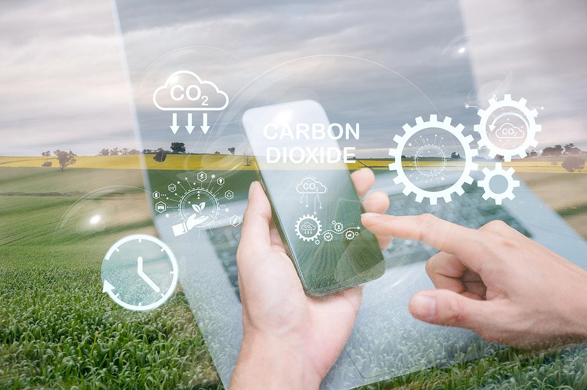 Smartphone displaying CO₂ data with digital graphics over farmland.